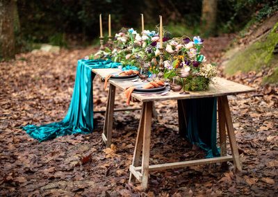 Mesa rústica decorada con flores, velas y telas verdes para una boda de otoño en el bosque