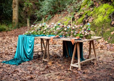 Mesa rústica decorada con flores, velas y telas verdes para una boda de otoño en el bosque