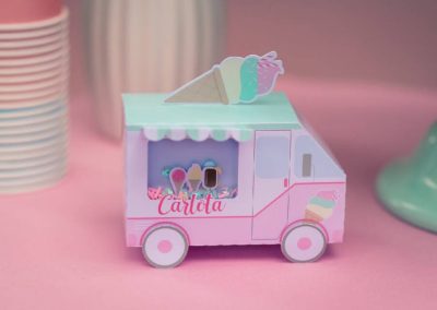 Caja decorativa infantil con forma de camión de helados personalizada con el nombre de Carlota sobre una mesa rosa