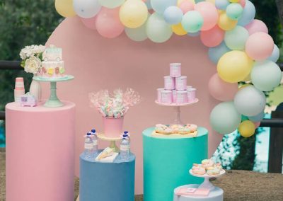 Mesa dulce de fiesta infantil con decoración en tonos pastel, globos de colores y soportes con dulces para la celebración de Carlota
